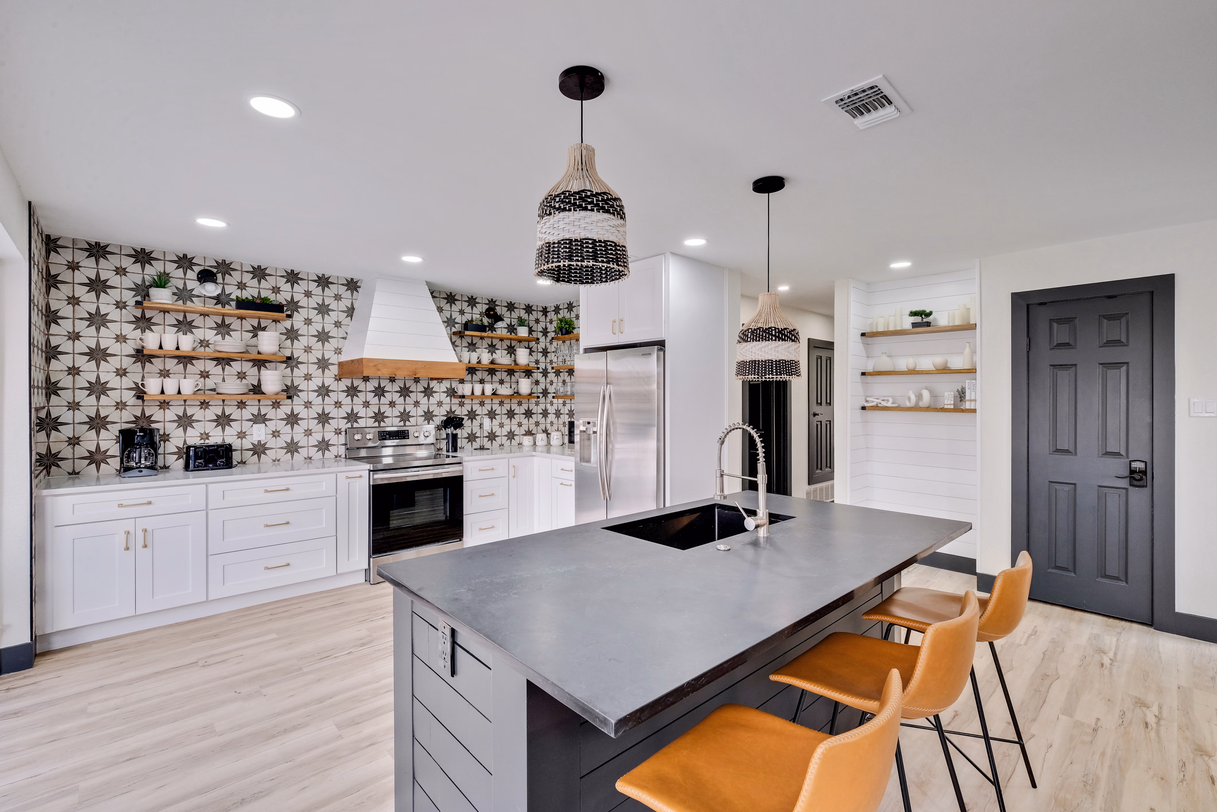 Kitchen — concrete island, range, white cabinets, bar stools.