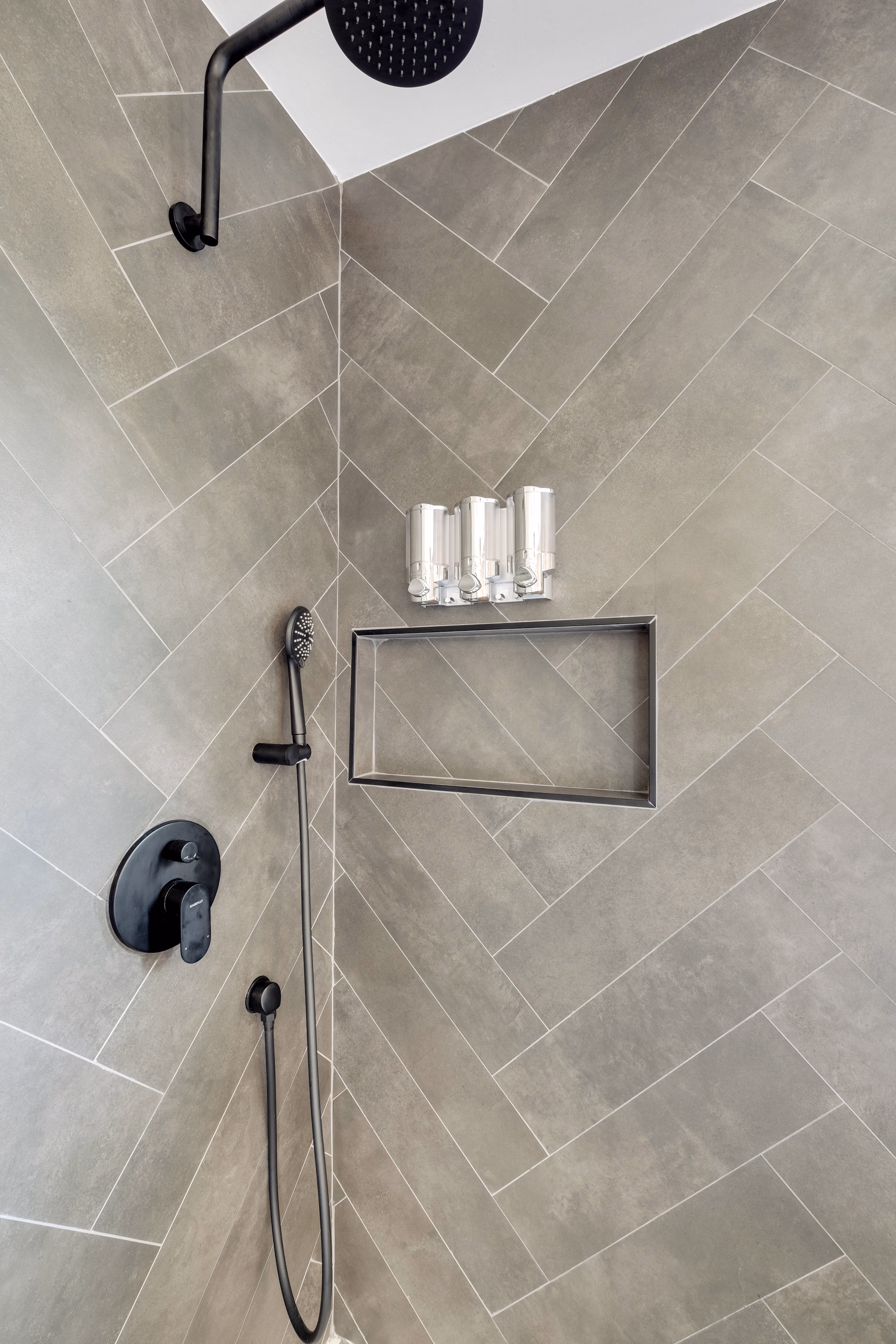 Shower detail — black rainfall head and herringbone tile niche.