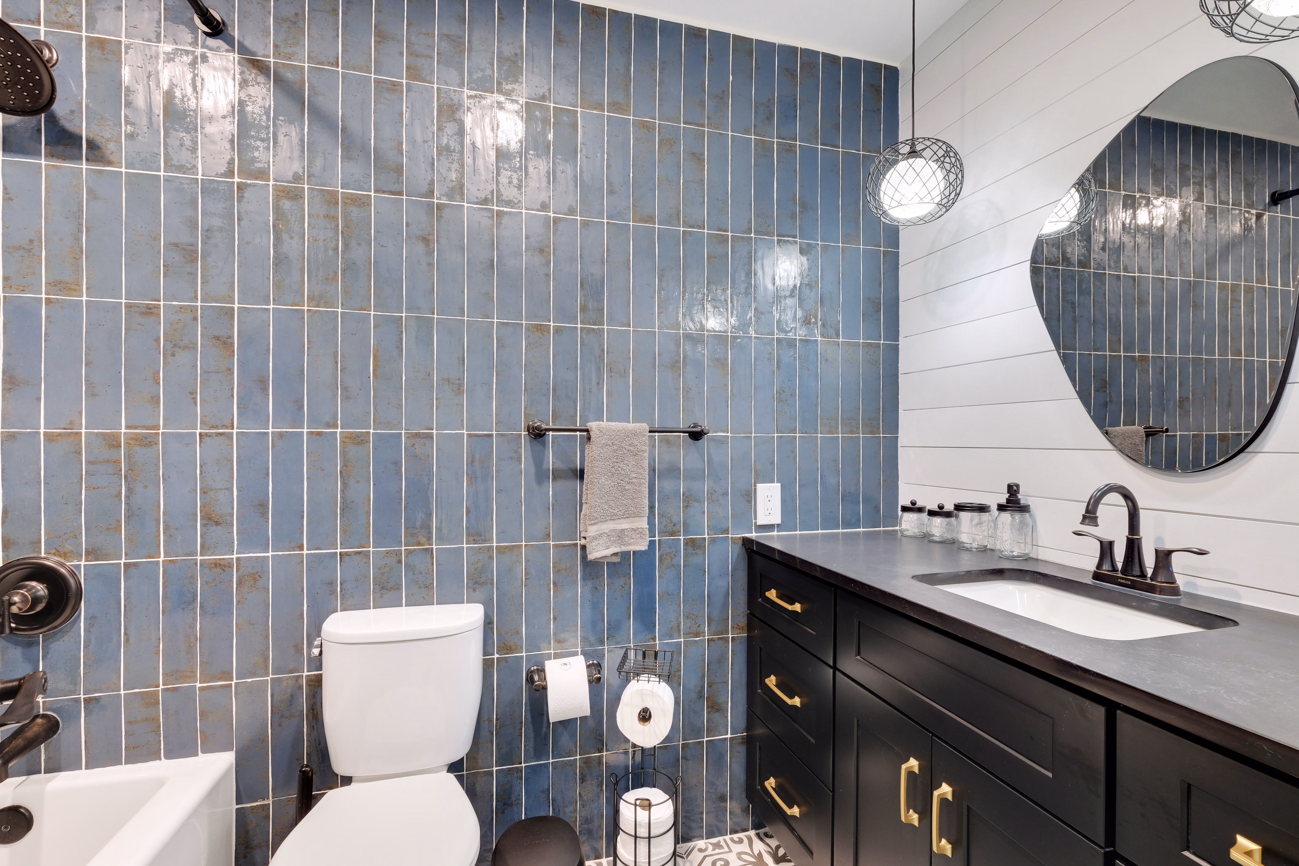 Bathroom — blue vertical tile, dark vanity, tub-shower combo.