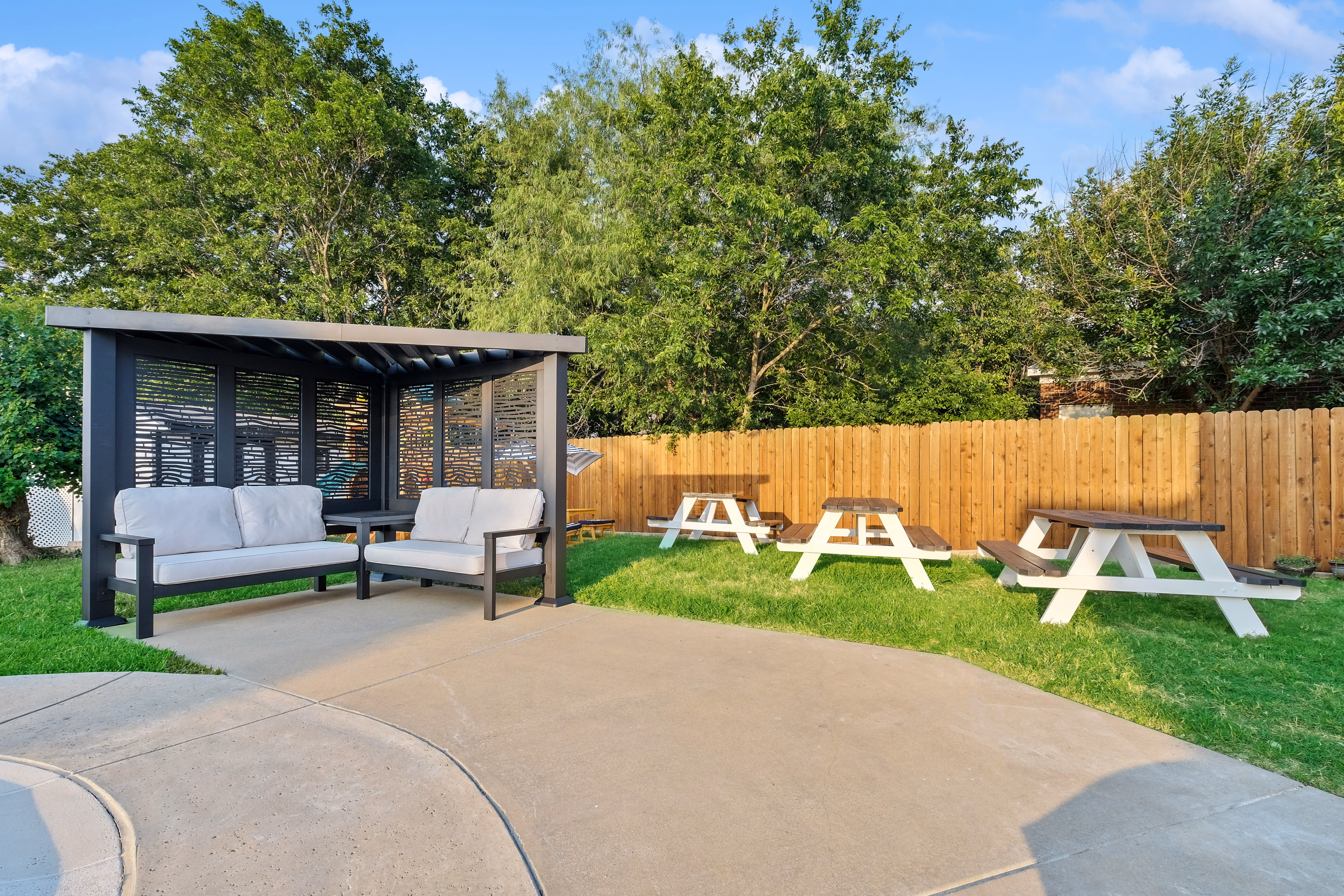 Cabana with sofa and chair facing three picnic tables on lawn.