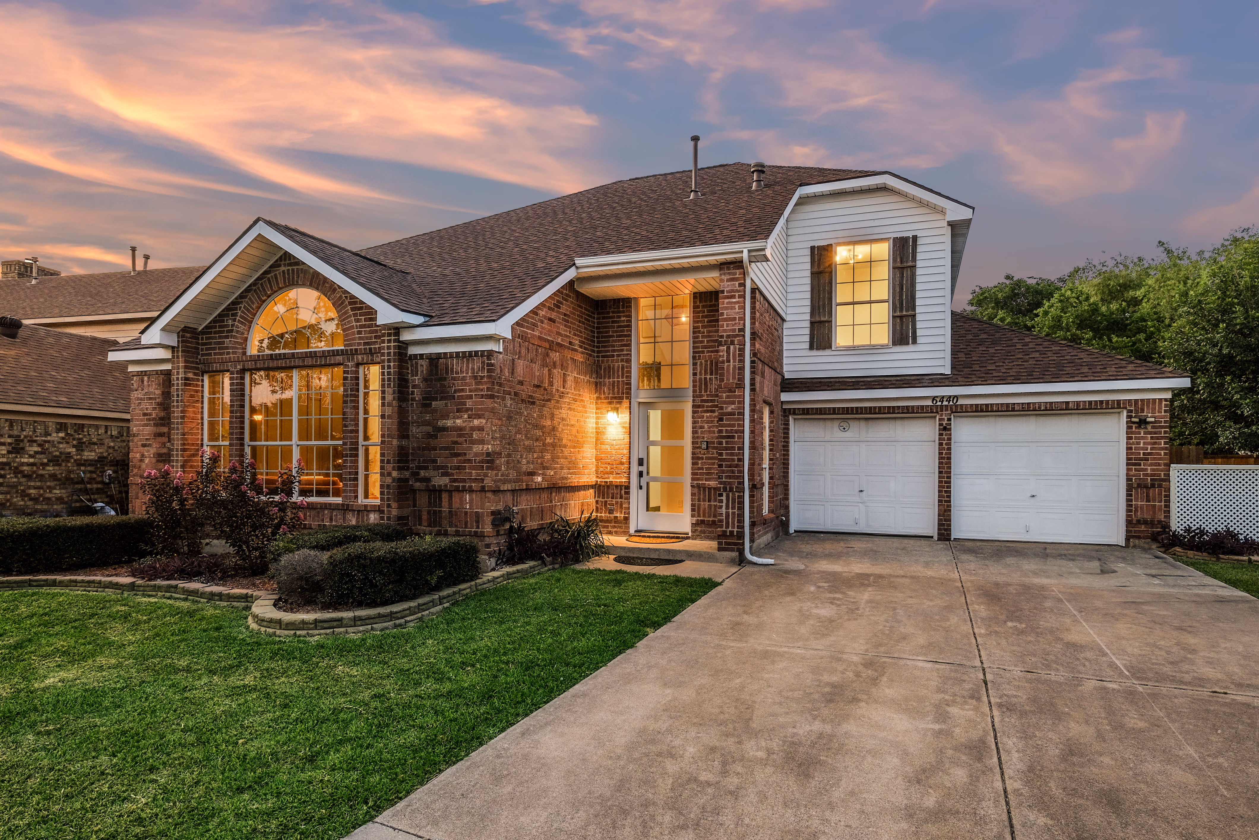 Front facade at dusk — warm interior glow, pink sky.