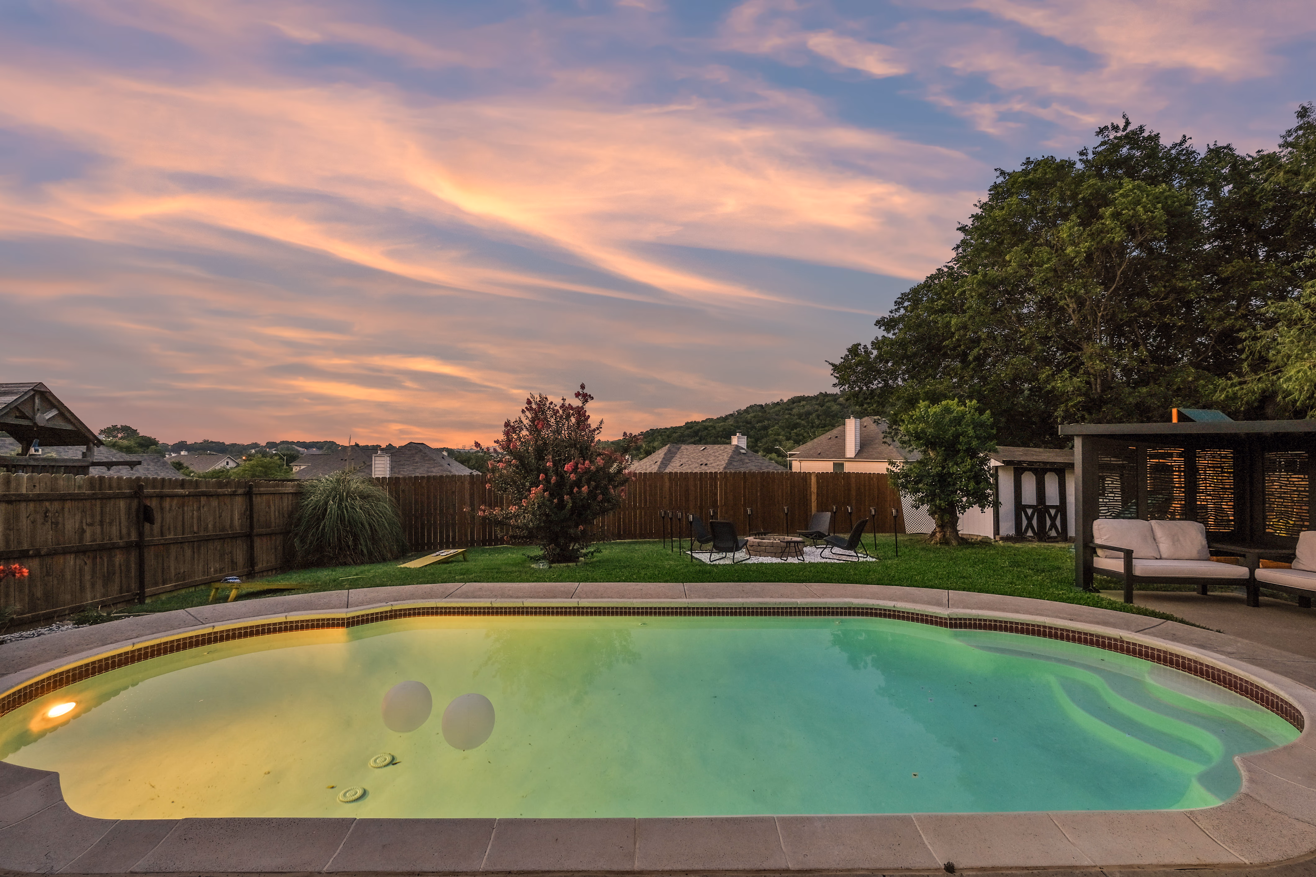 Pool at twilight with glowing water, hills, and pink sky.