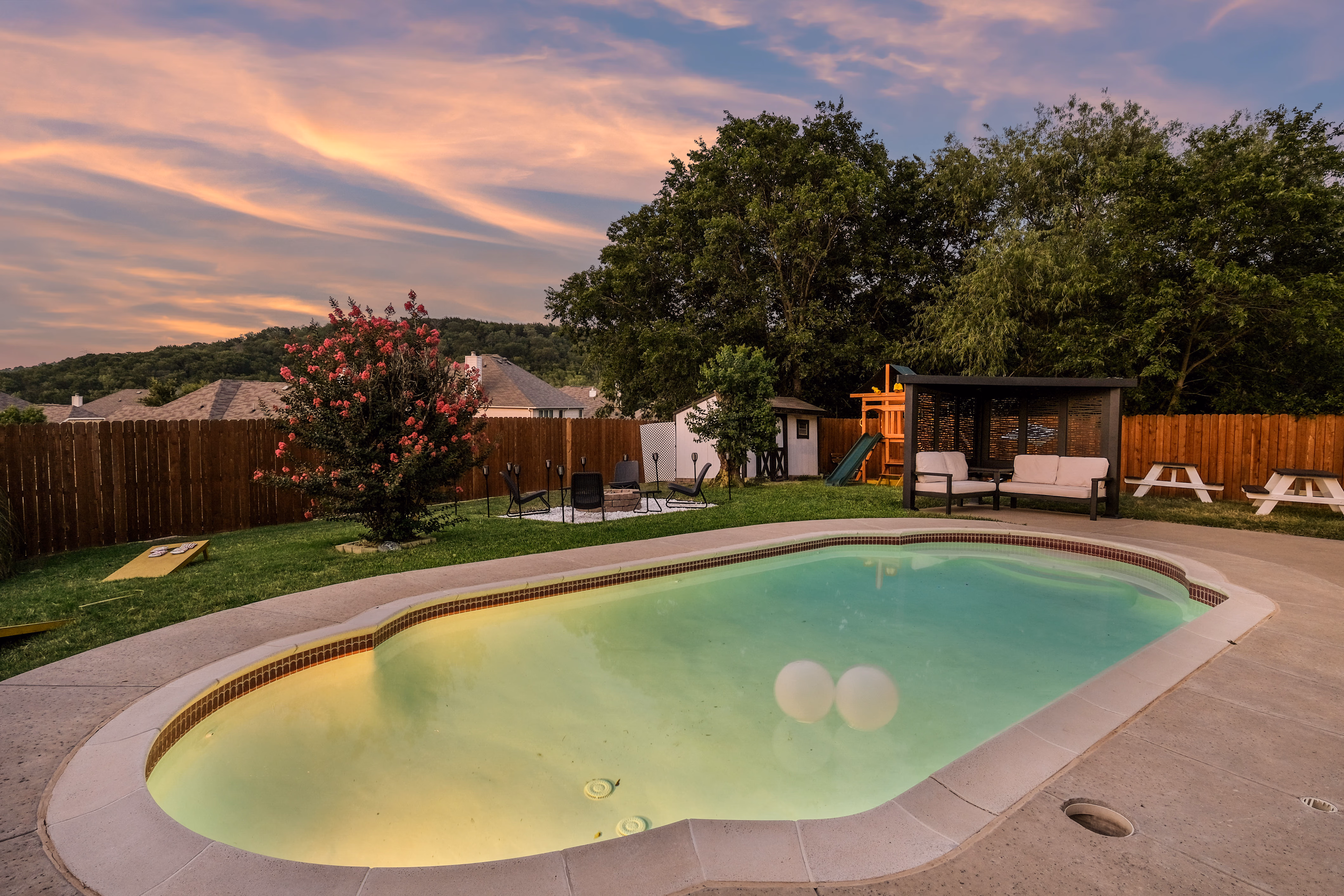 Pool, cabana and playset at twilight under pastel sky.