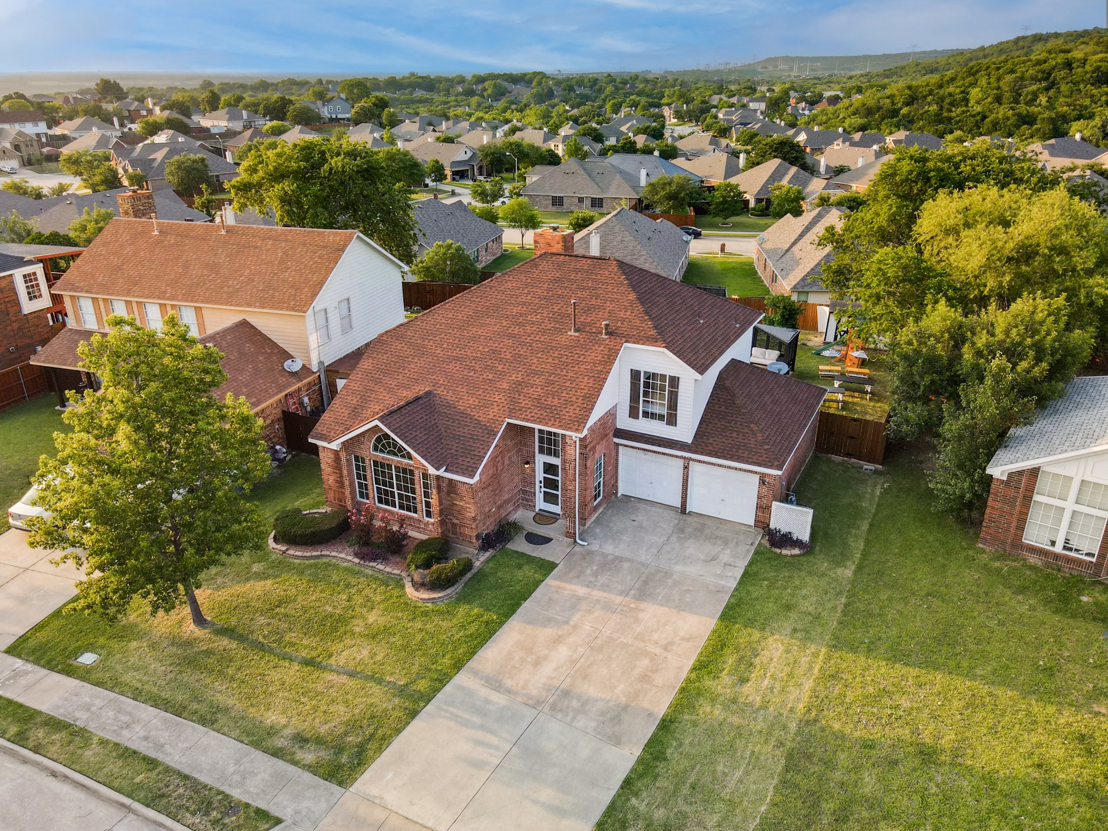 Aerial front — roof and lawn from above, distant hills.